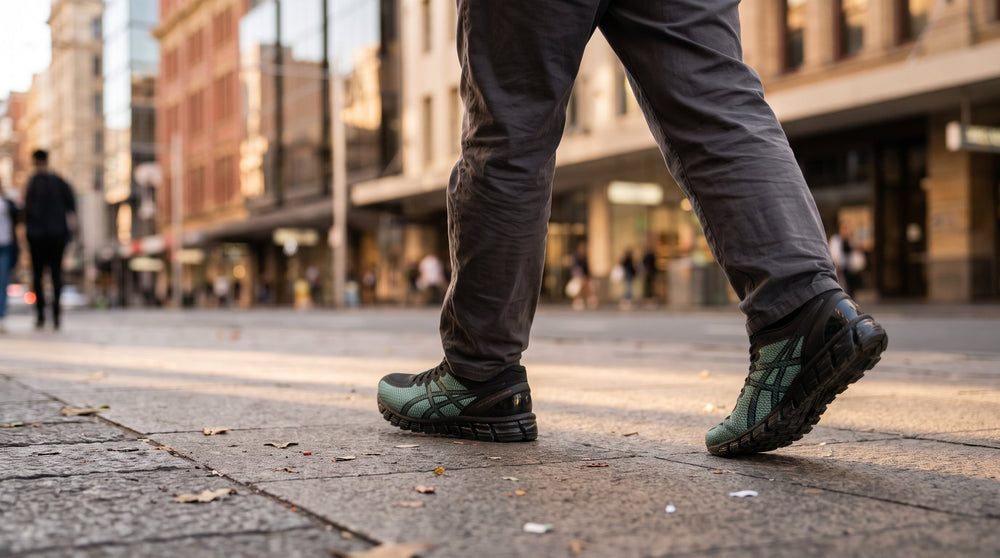 Person walking along a city footpath wearing green and black ASICS running shoes with mesh uppers