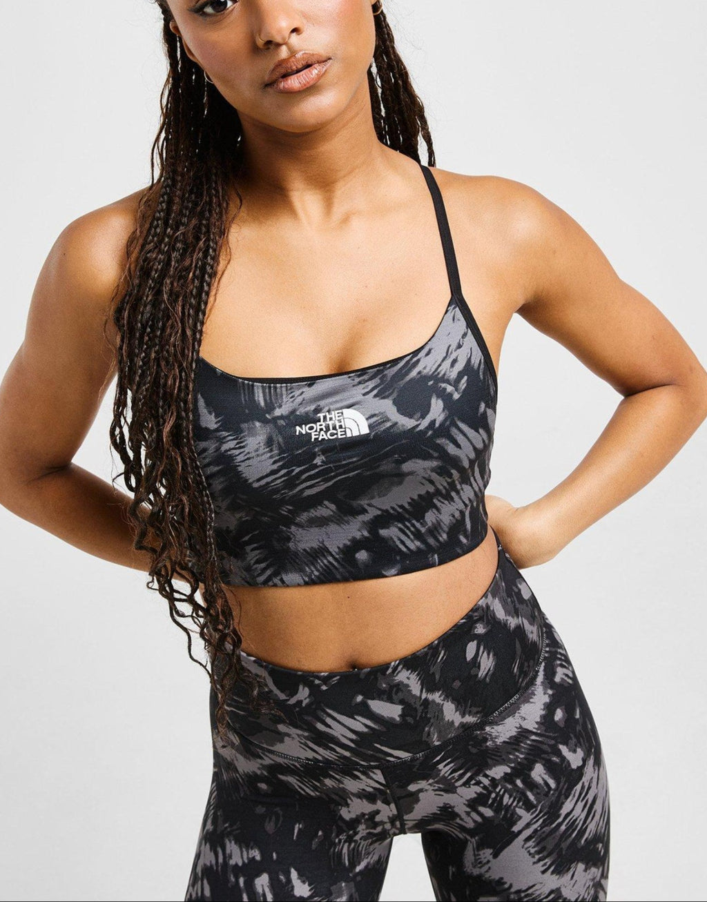 Woman wearing a black and gray patterned sports bra and leggings set on a white background